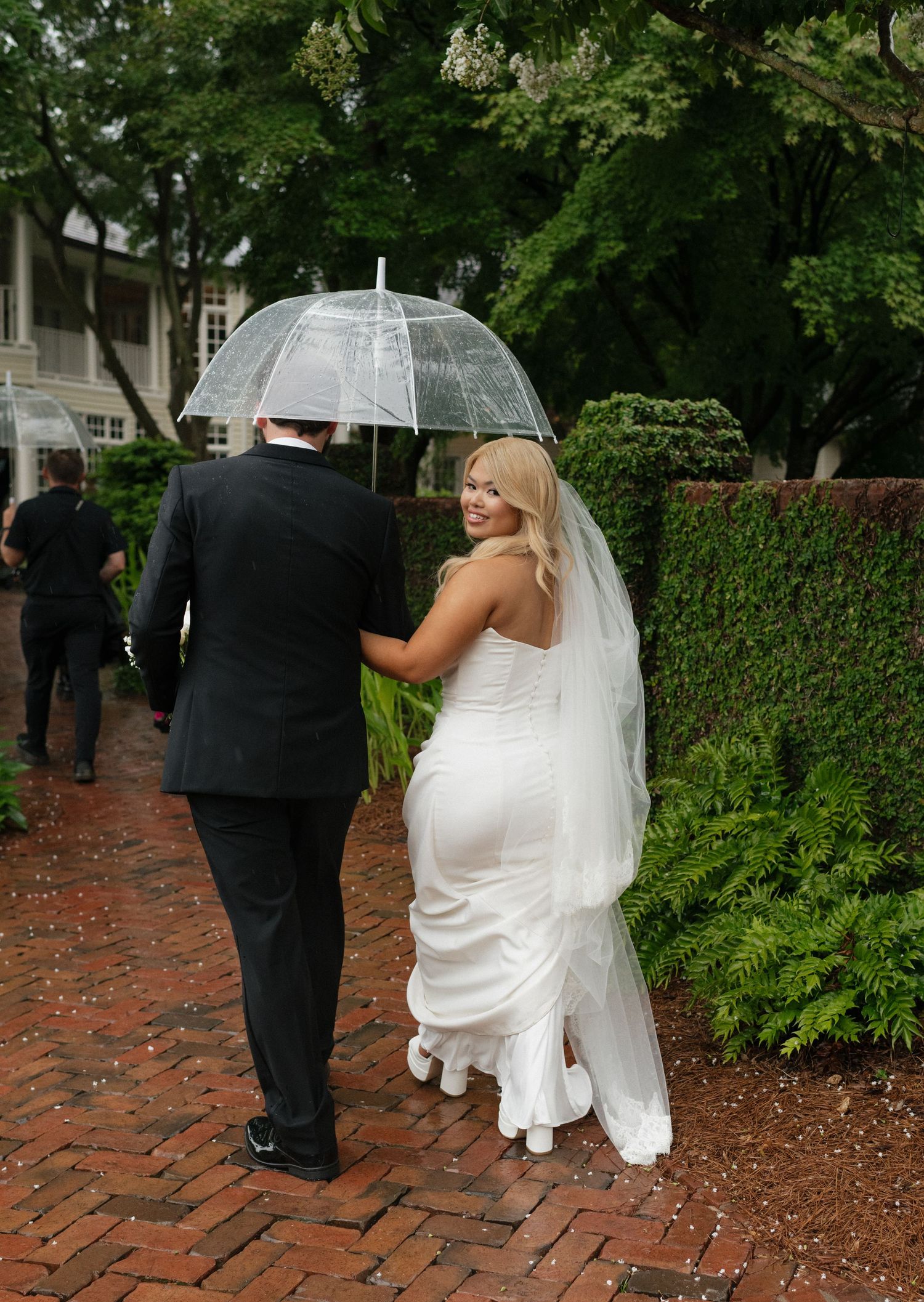 Couples walk along a brick pathway surrounded by lush green landscaping.