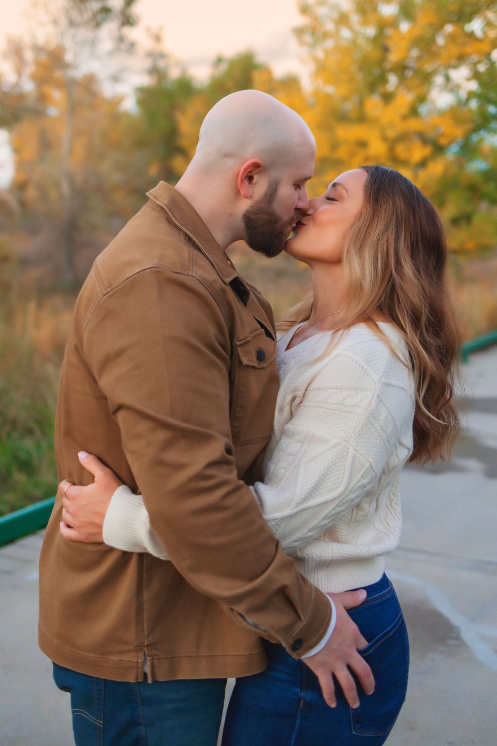 A romantic couple embraces and kisses in a fall setting with golden leaves in the background.