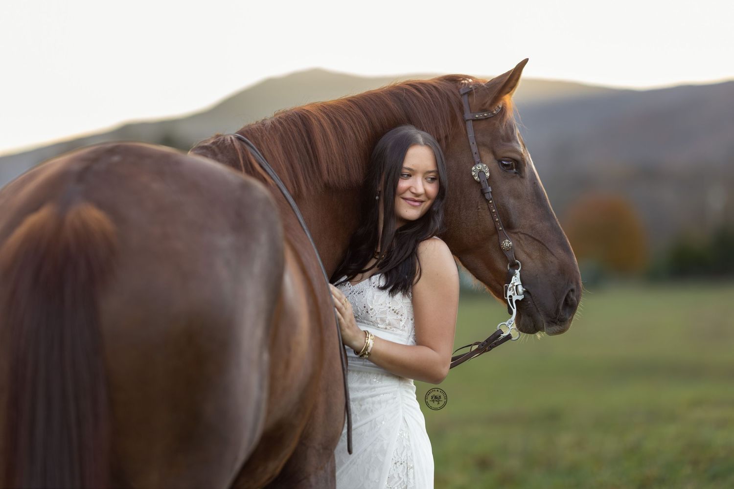A person in black attire tends to a chestnut horse in an indoor riding arena with sandy ground.