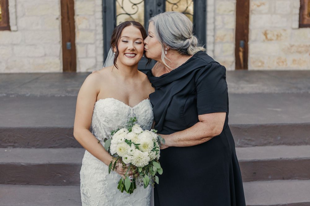 A tender moment between a bride in a white gown and someone in black during an outdoor wedding celebration.