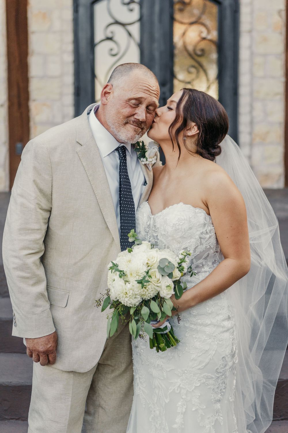 Wedding couple shares intimate moments against a stone building backdrop.