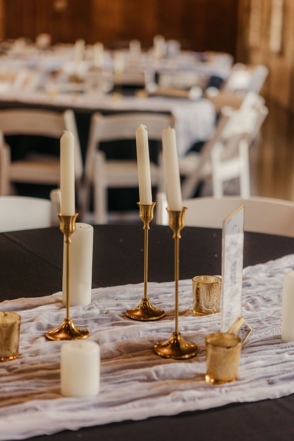 Elegant white candles in gold holders arranged on a rustic table runner for wedding reception.
