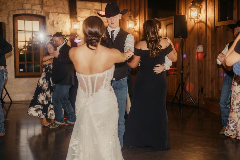 A couple shares their first dance at a rustic barn wedding reception illuminated by warm glowing lights.
