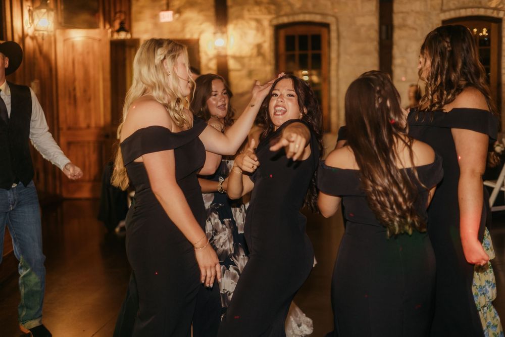 People in black attire dancing and celebrating at an elegant indoor venue with warm lighting and stone walls.