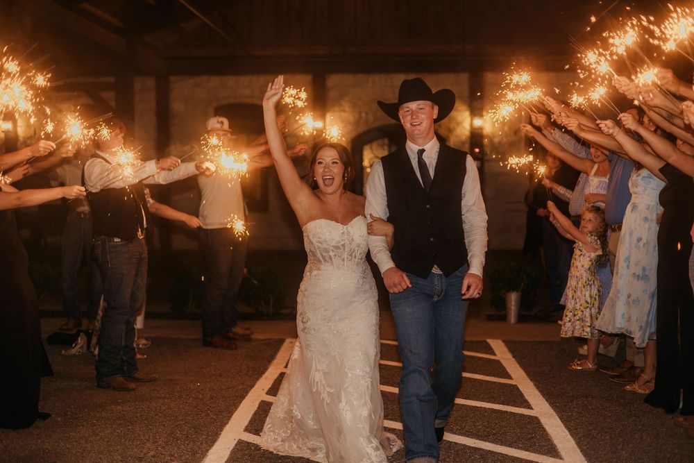 A couple exits their wedding celebration through a sparkler tunnel held by guests at night.