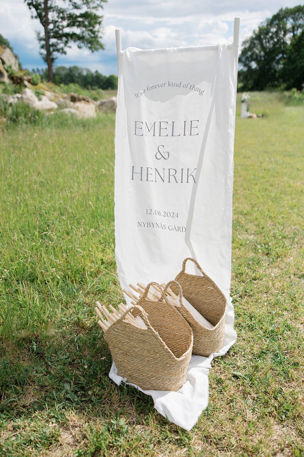 White paper bags with names and woven straw shoes arranged on grass for a rustic outdoor wedding display.