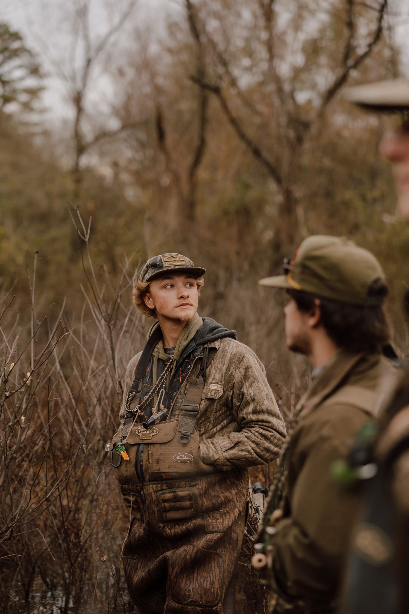Hunters in camouflage gear and caps stand together in a wooded area during hunting season.