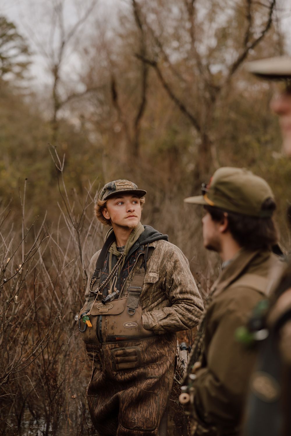 Hunters in camouflage gear and caps stand together in a wooded area during hunting season.