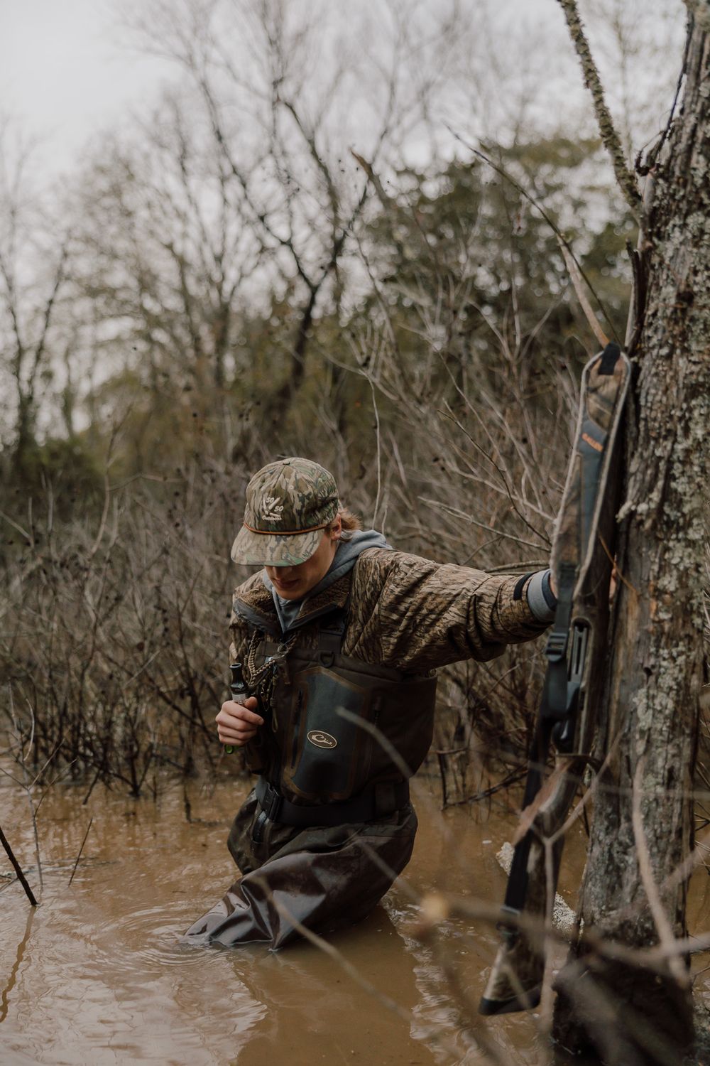 Duck hunter crouches in flooded timber while hunting waterfowl during winter season.