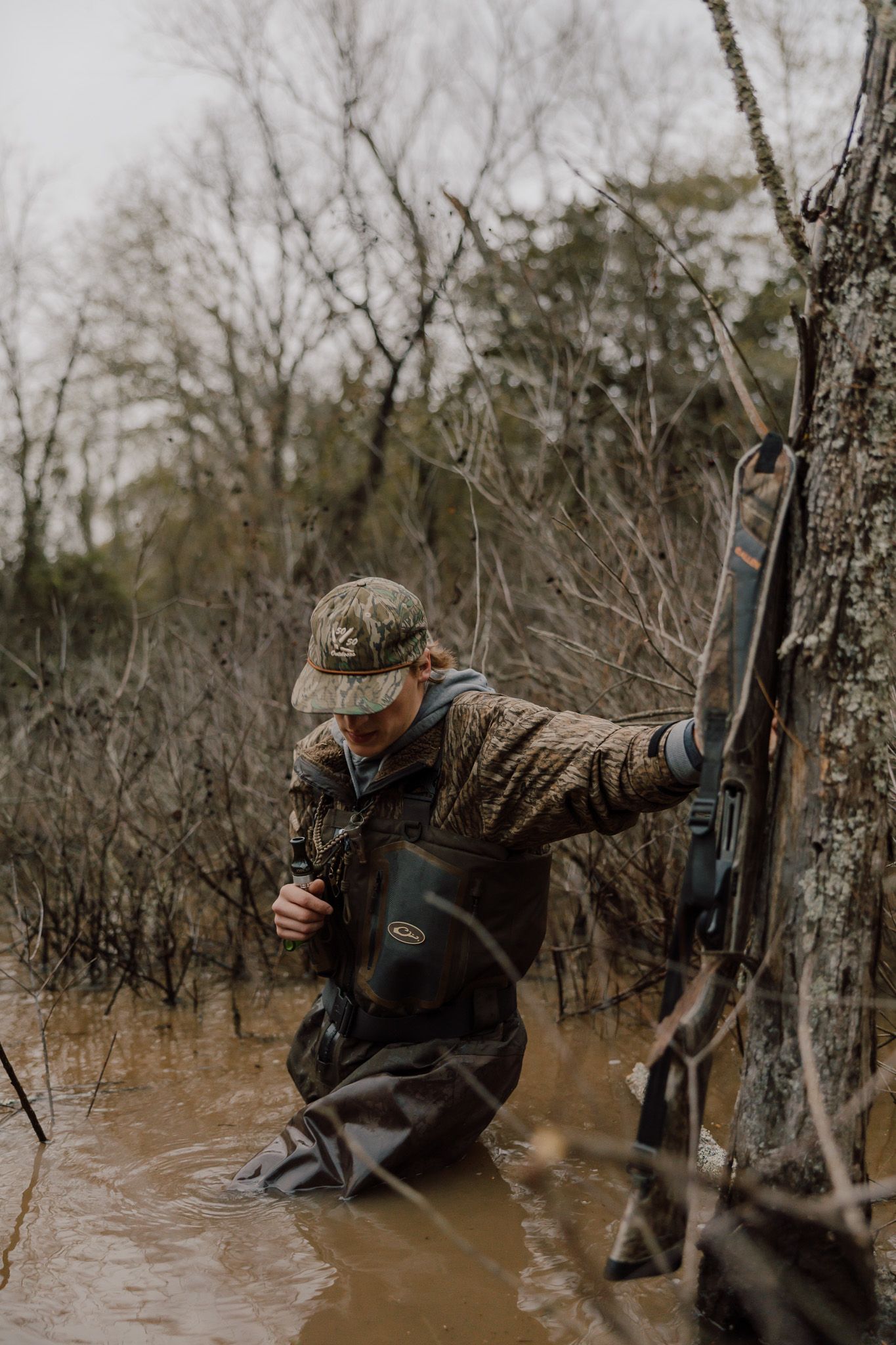 Duck hunter crouches in flooded timber while hunting waterfowl during winter season.