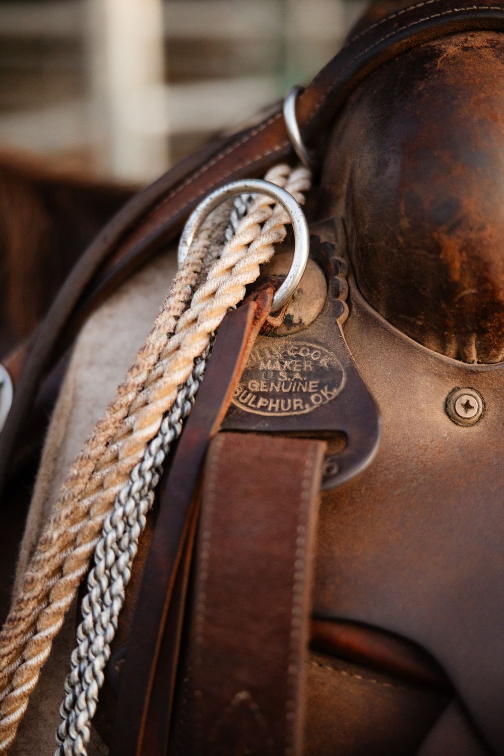 Close-up detail of a brown leather saddle showing decorative stitching, metal hardware and rope detail.