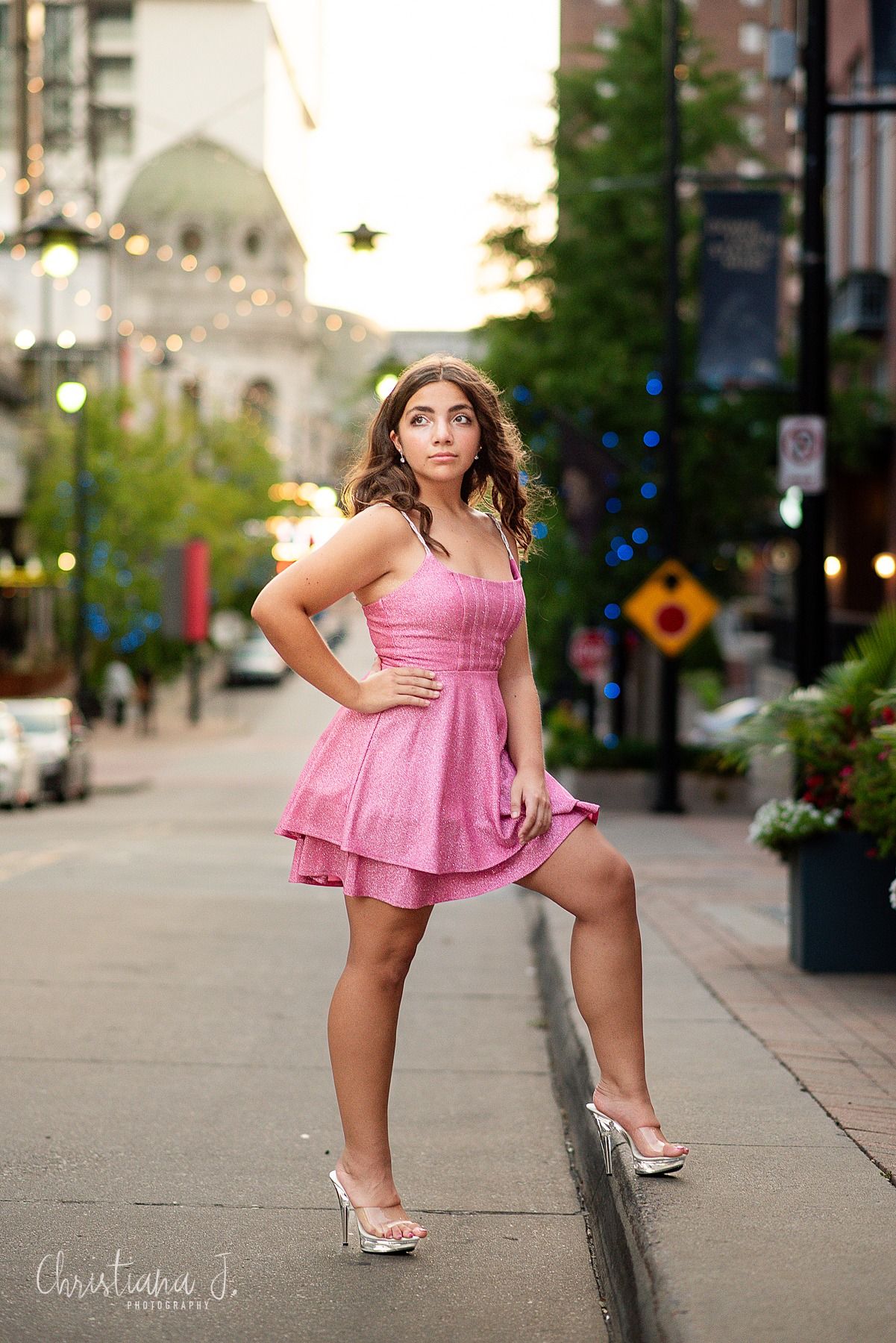 High school senior photographer kansas city, girl in a pink dress and heels poses in the street at sunset with an urban backdrop downtown KC