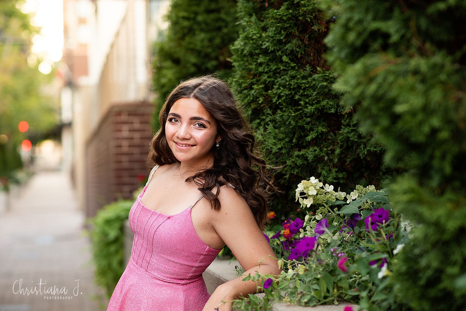 High school senior photographer Kansas City, girl in a pink dress poses outdoors against a natural backdrop with lush greenery and flowers.