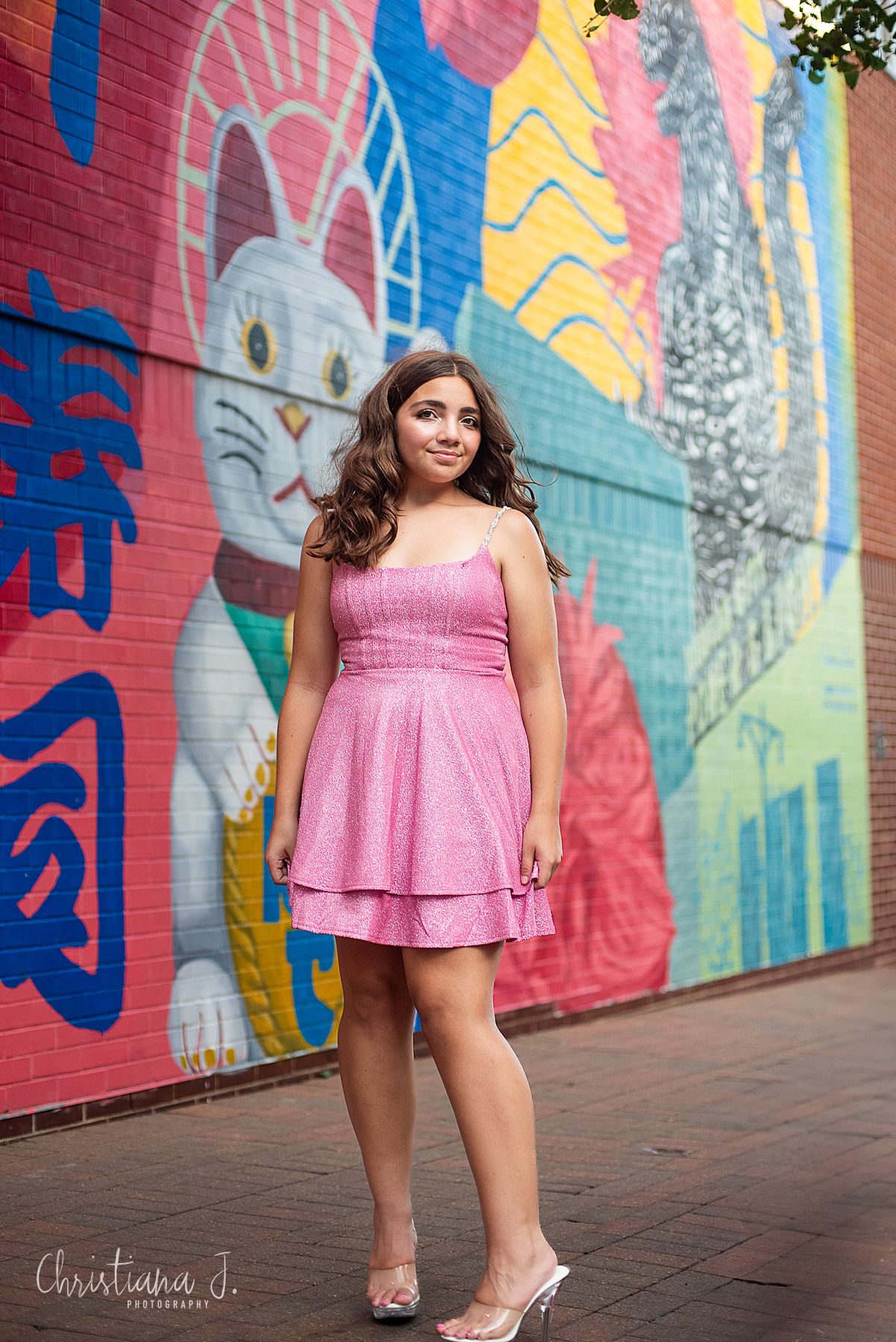 High school senior photographer Kansas city, girl pink dress and heels pose near a colorful art mural with a cat in power and light district