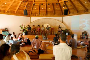 Participants seated in circular formation inside wooden domed room with projection screen.