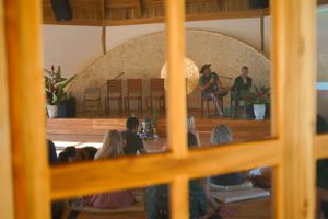 View through window panes of people gathered in a wooden domed room with warm lighting.