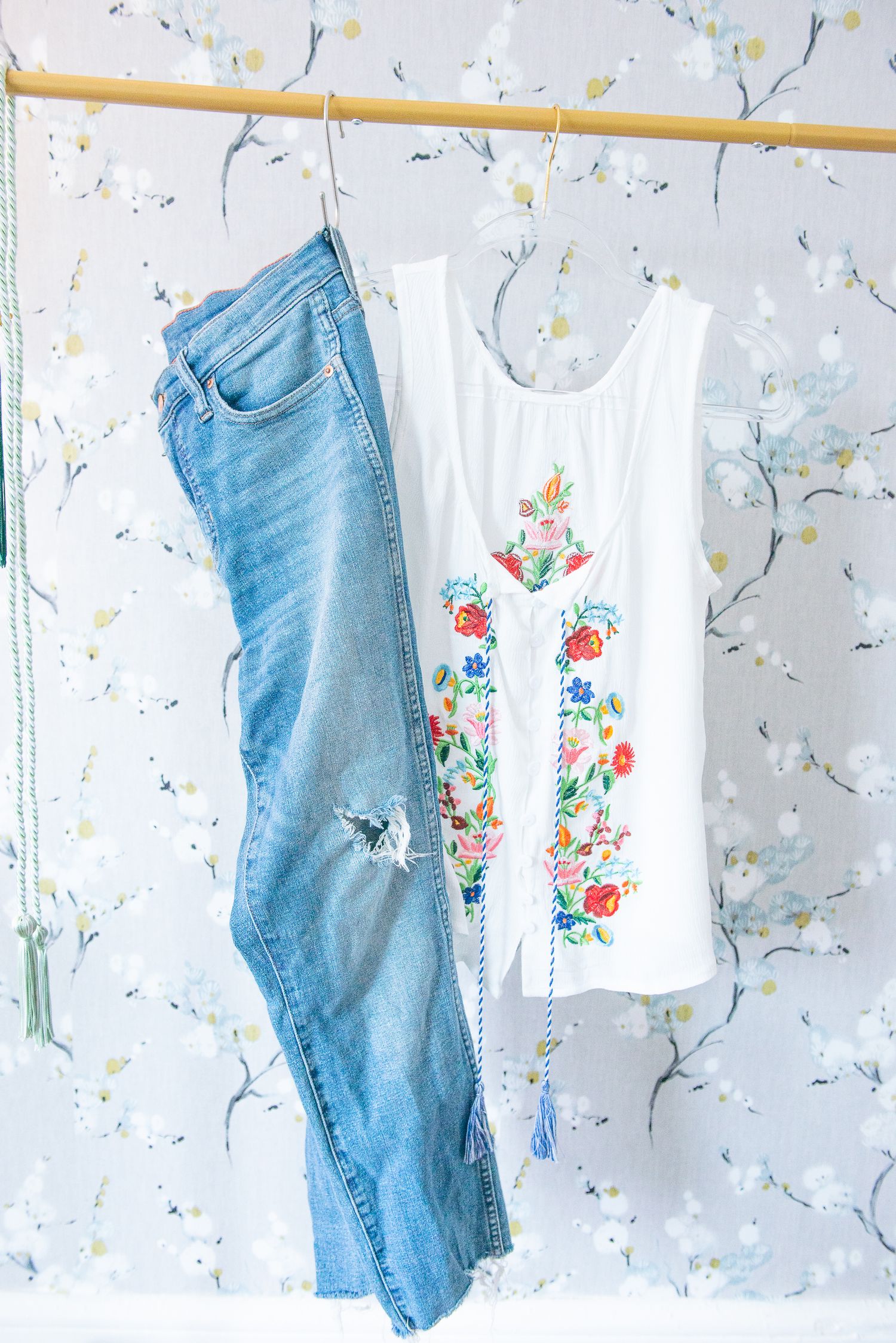 Baby clothes and denim jeans hanging to dry on a clothesline against floral wallpaper background.