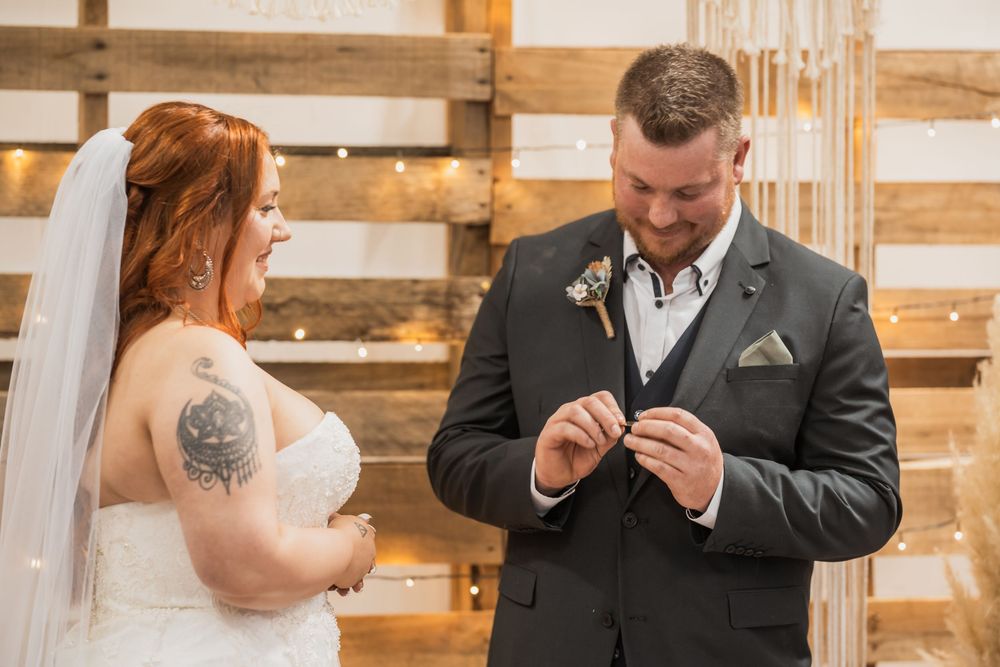A couple shares an intimate wedding ceremony moment in front of a rustic wooden wall backdrop.