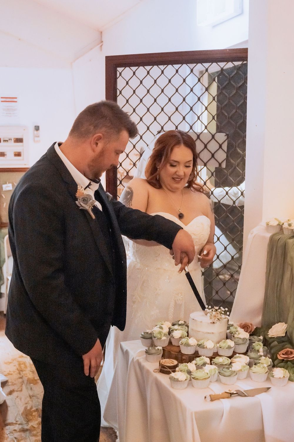 A bride and groom share a sweet moment while cutting their wedding cake decorated with white frosting and flowers.