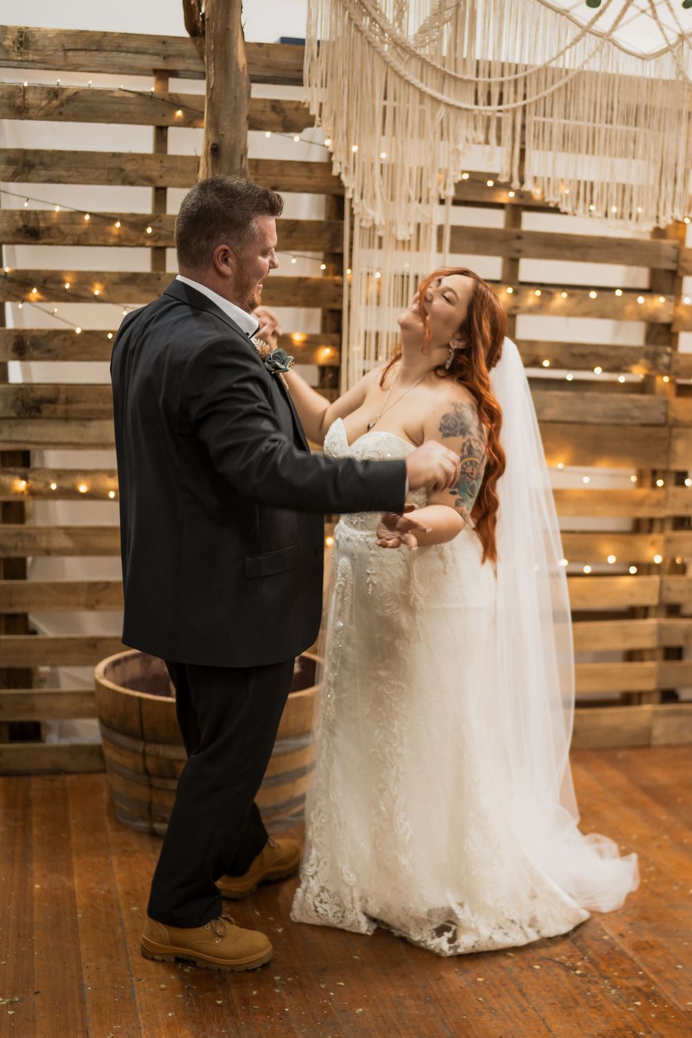 Light-filled rustic barn wedding venue with romantic string lights and wooden pallet wall during first dance moment.