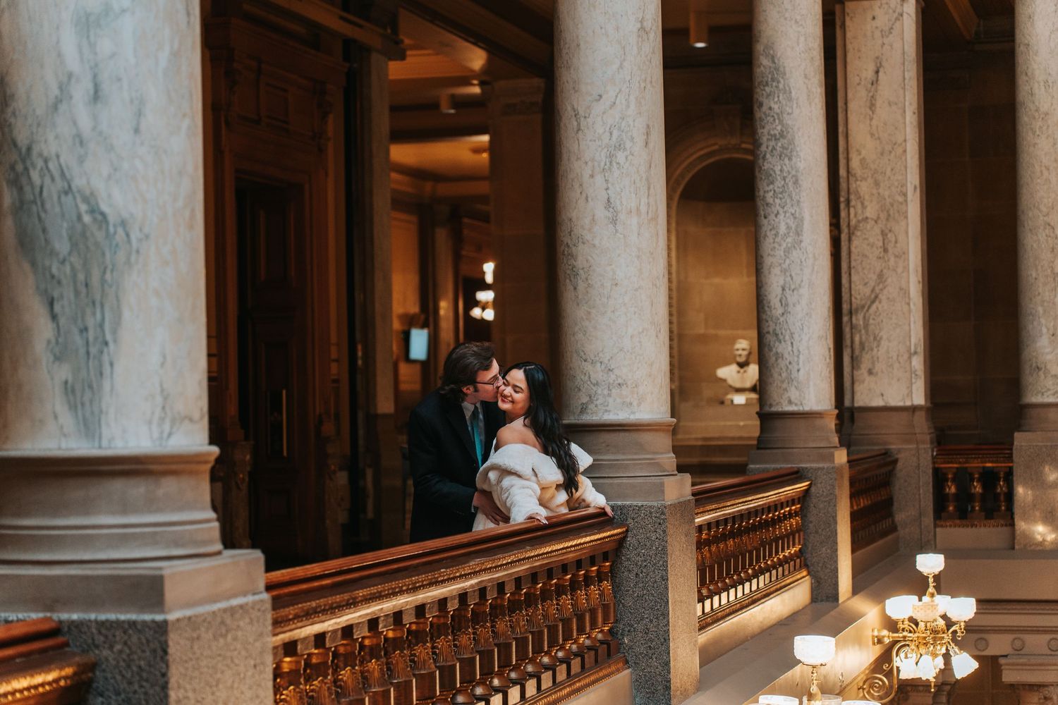 Couple sharing intimate moment between elegant classical columns in historic building.