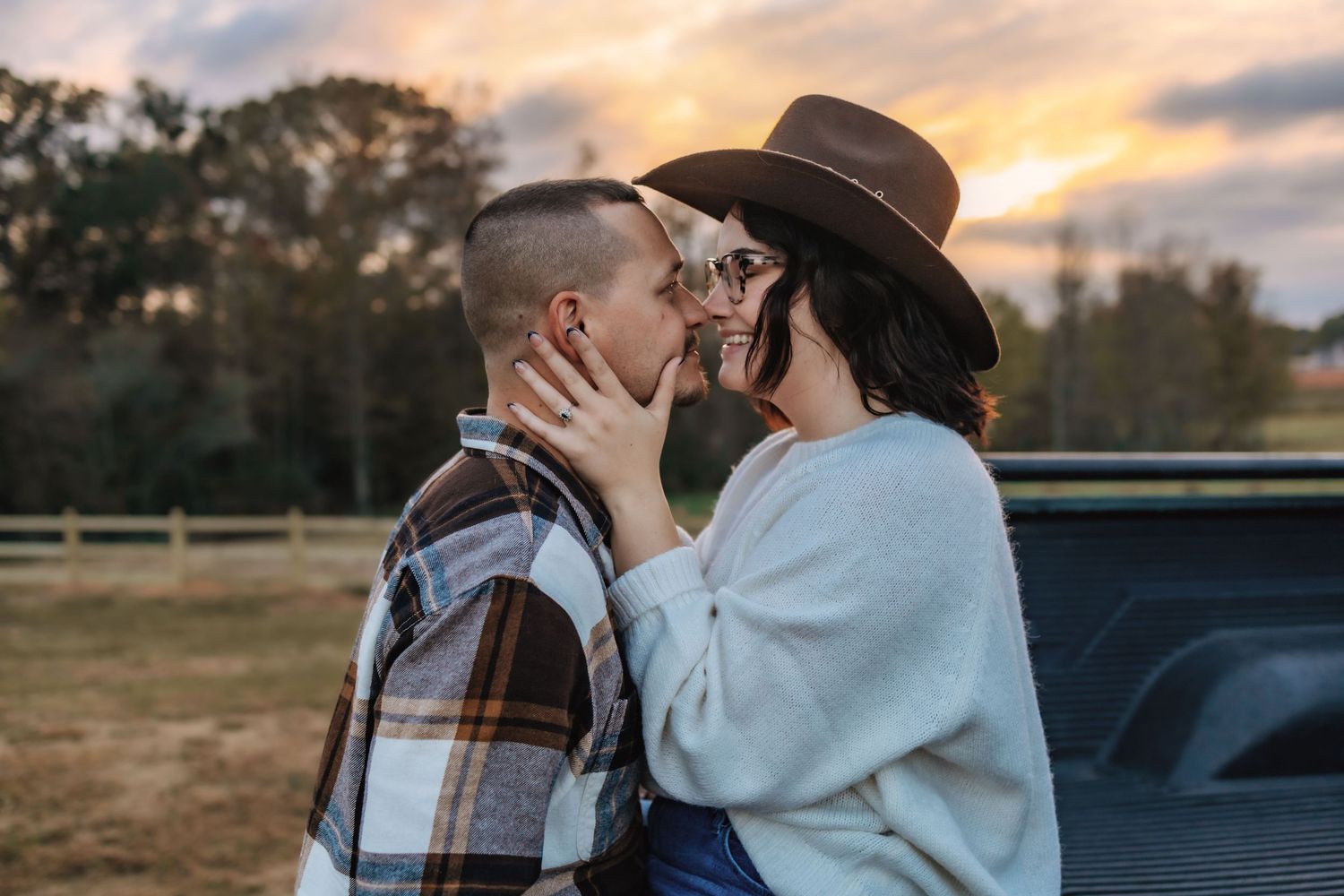 A romantic couple embrace in a series of sunset photos against a rustic countryside backdrop.