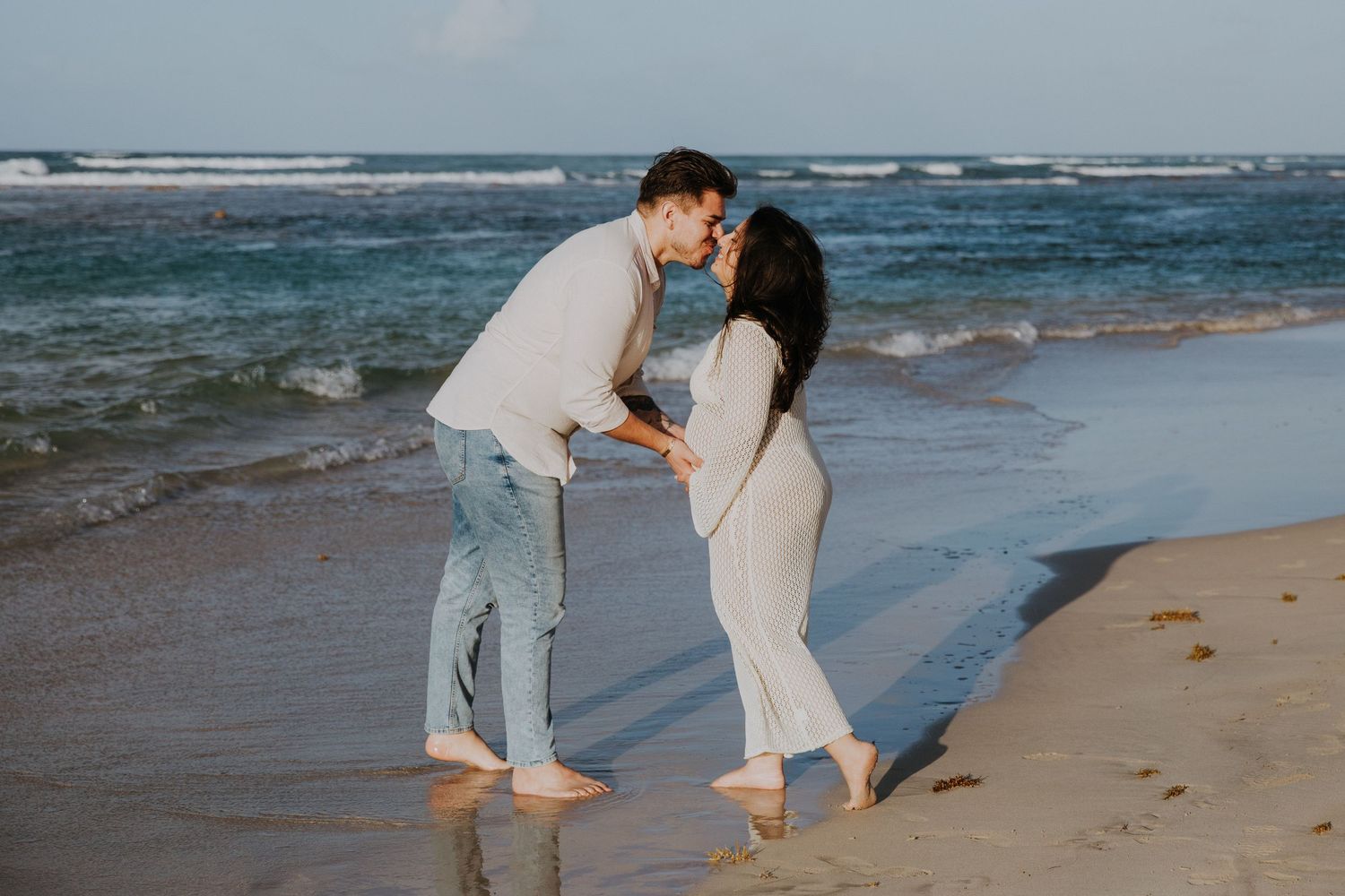 A tender moment shared between a couple standing on a sandy beach near the ocean.
