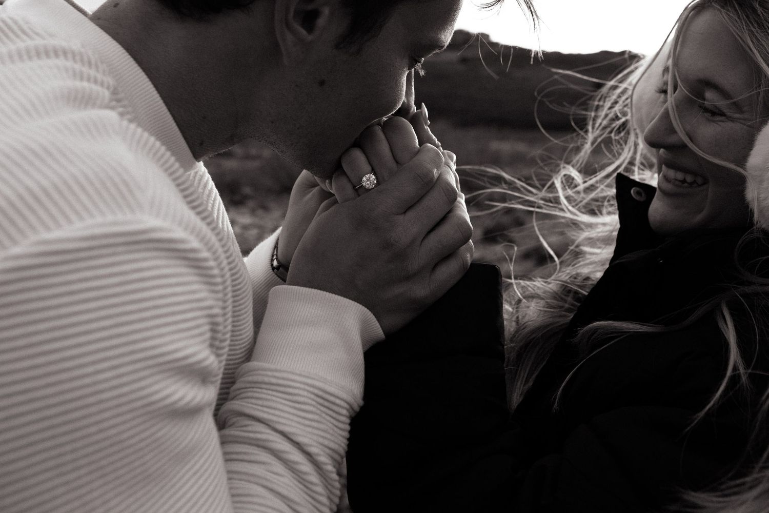 Engagement ring shot where man warms girls hands with a kiss