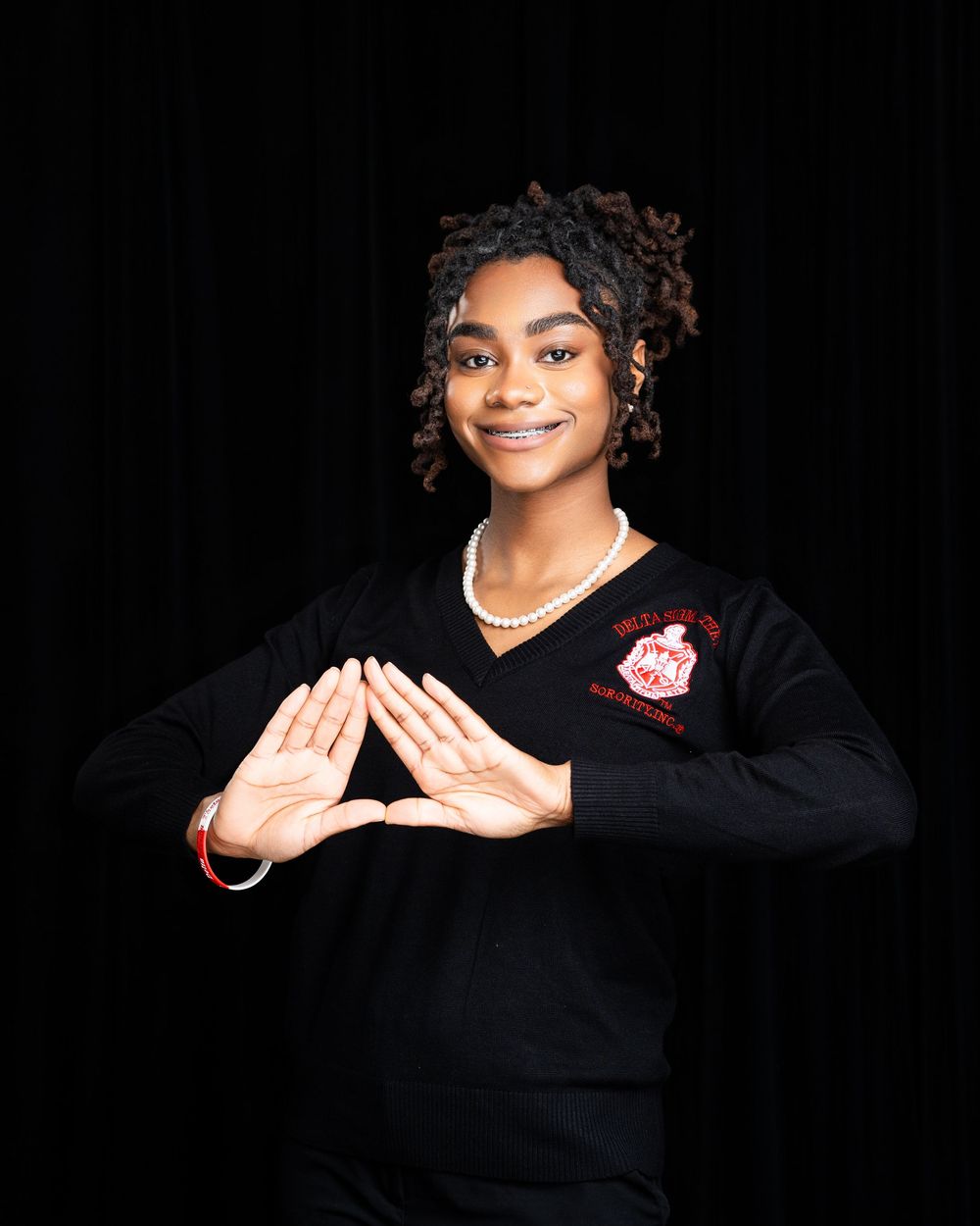 Studio portraits showing hand gestures against black background wearing black sweater.