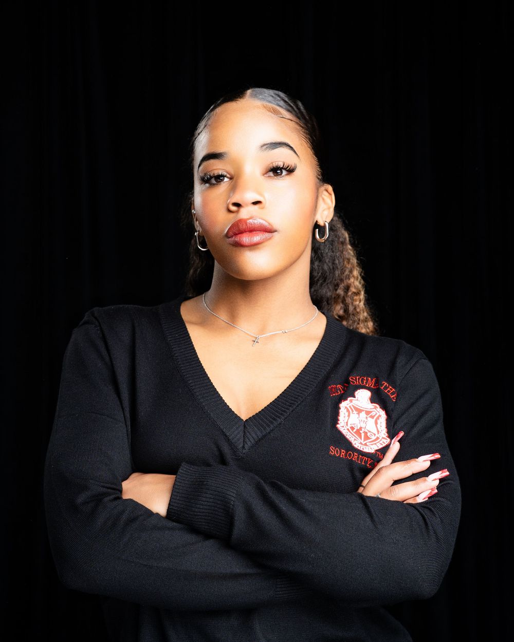 Professional portrait of someone in a black v-neck sweater with crossed arms against dark background.