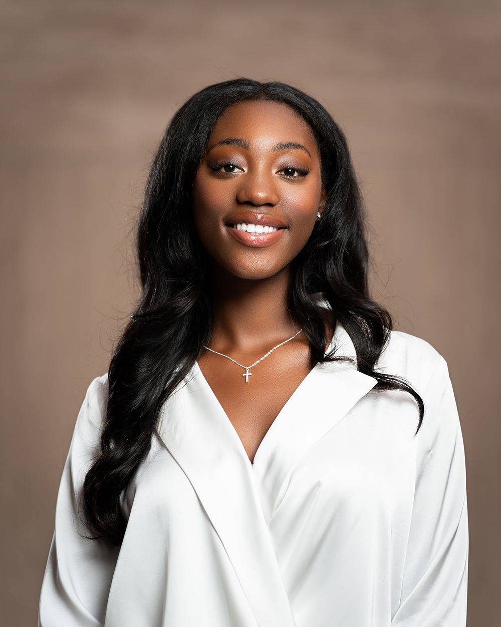 Professional portrait of someone in white blouse with long dark hair against neutral background.