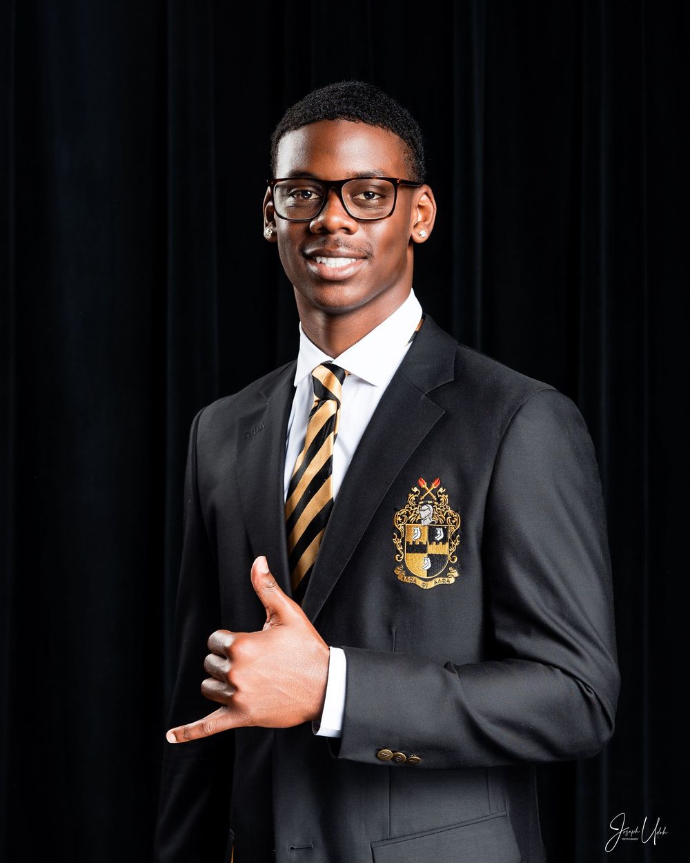 Professional portrait of student in glasses wearing black blazer with striped tie and school crest.