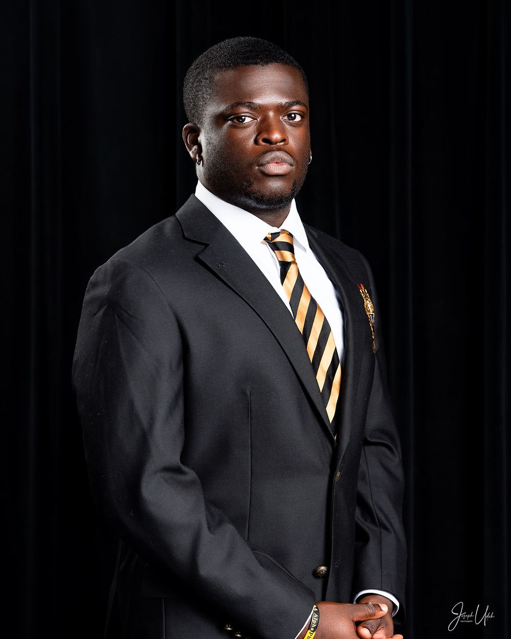Portrait of student in formal attire with striped tie and blazer featuring school insignia.