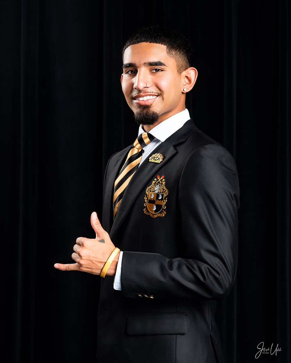 Portrait of student giving thumbs up while wearing dark blazer with striped tie and school crest.