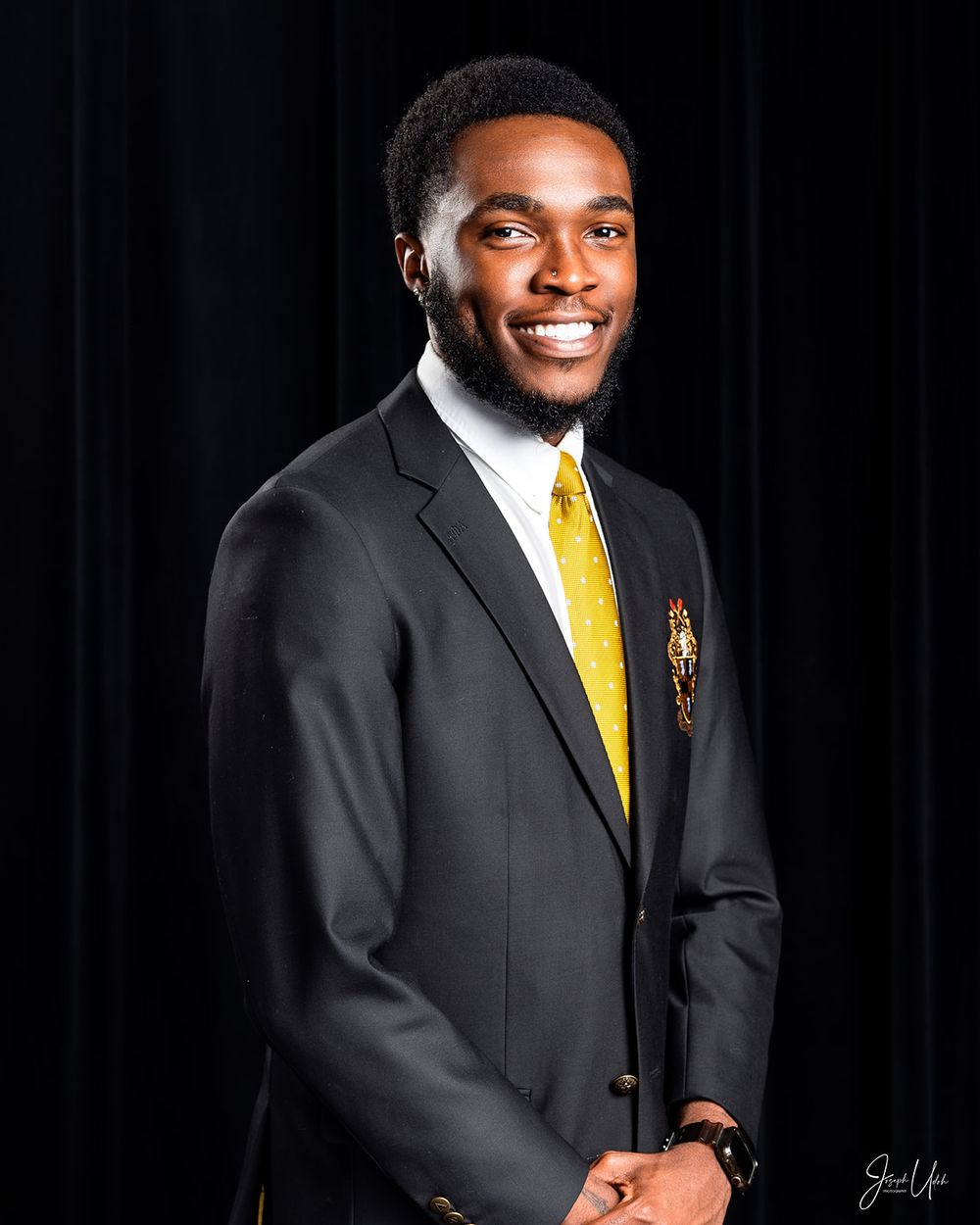 Professional headshot of student in dark suit with yellow tie and school emblem.