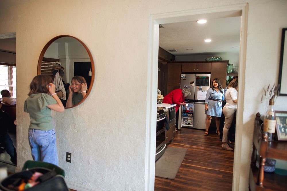 A small gathering of people in a modern living space with hardwood floors and decorative mirror on the wall.