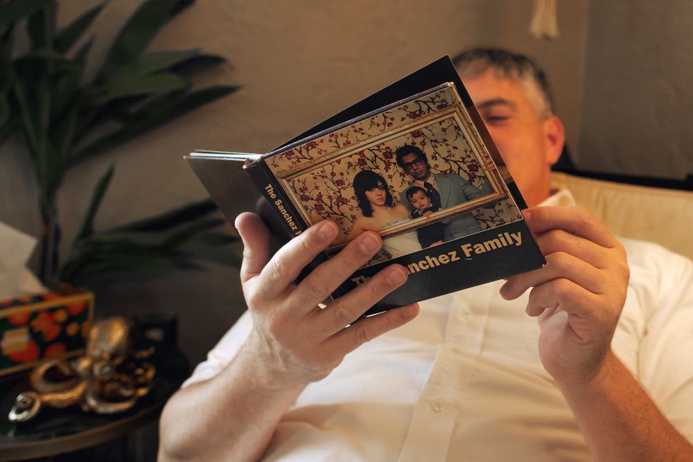 A person relaxes while reading a vintage hardcover book in bed next to a houseplant.
