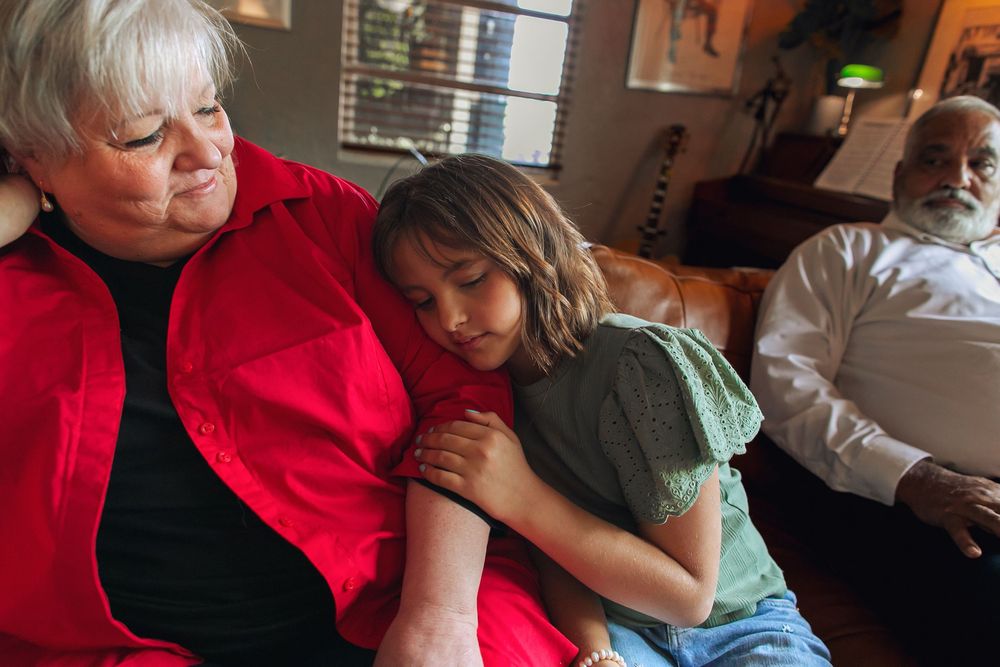 Adult and child sharing tender moment while embracing on couch in red and green clothing.