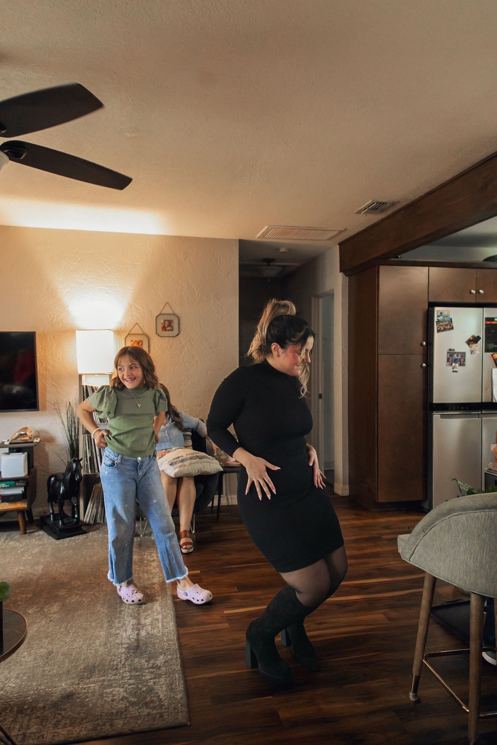 A group practices dance moves together in a dimly lit indoor space with wooden floors and modern furniture.