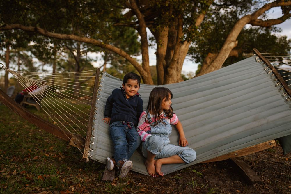 Two people relaxing together in a large hammock suspended between trees at sunset.