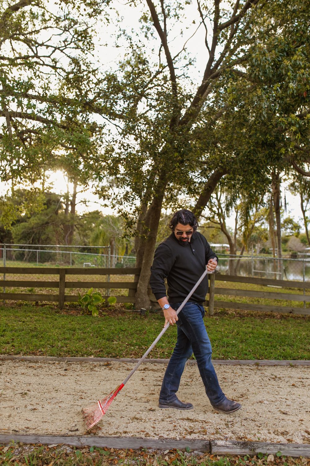 Someone using a rake to clean up leaves and debris in a park-like setting during late afternoon sunlight.