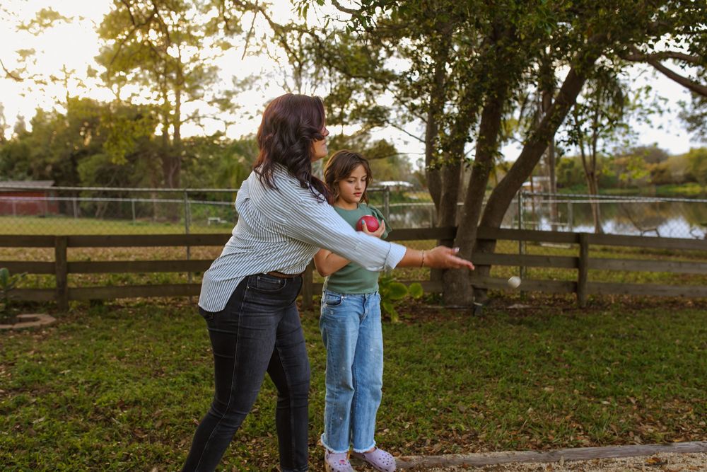 Two people share an outdoor moment together by a wooden fence at sunset near a pond.