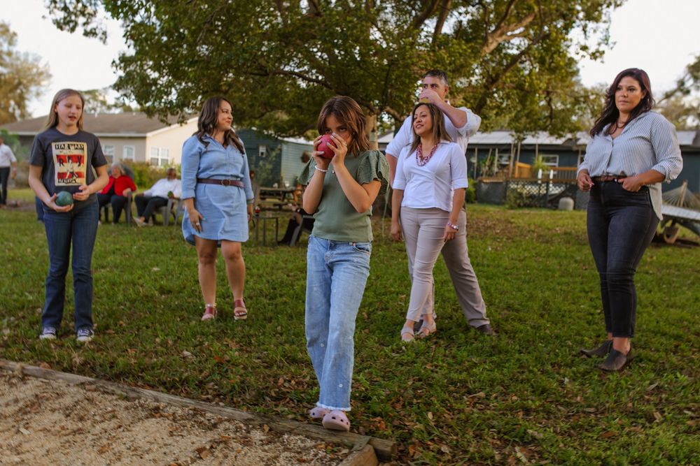 Group of people standing on grass at an outdoor gathering at sunset during autumn.