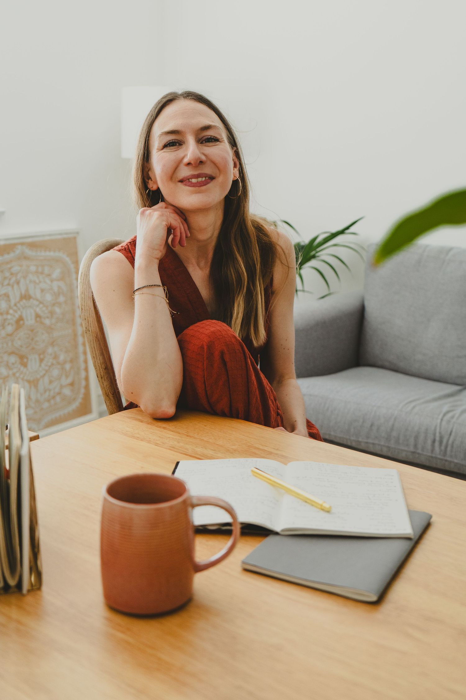 Brand portrait for female VA. A cosy home office, brown dress, cup, notebooks and indoor plants on a wooden table.