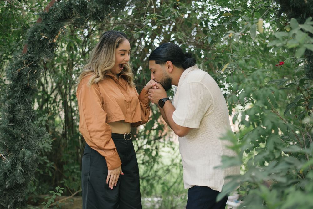 A couple shares a tender moment in a garden setting while wearing casual outfits of peach and white.
