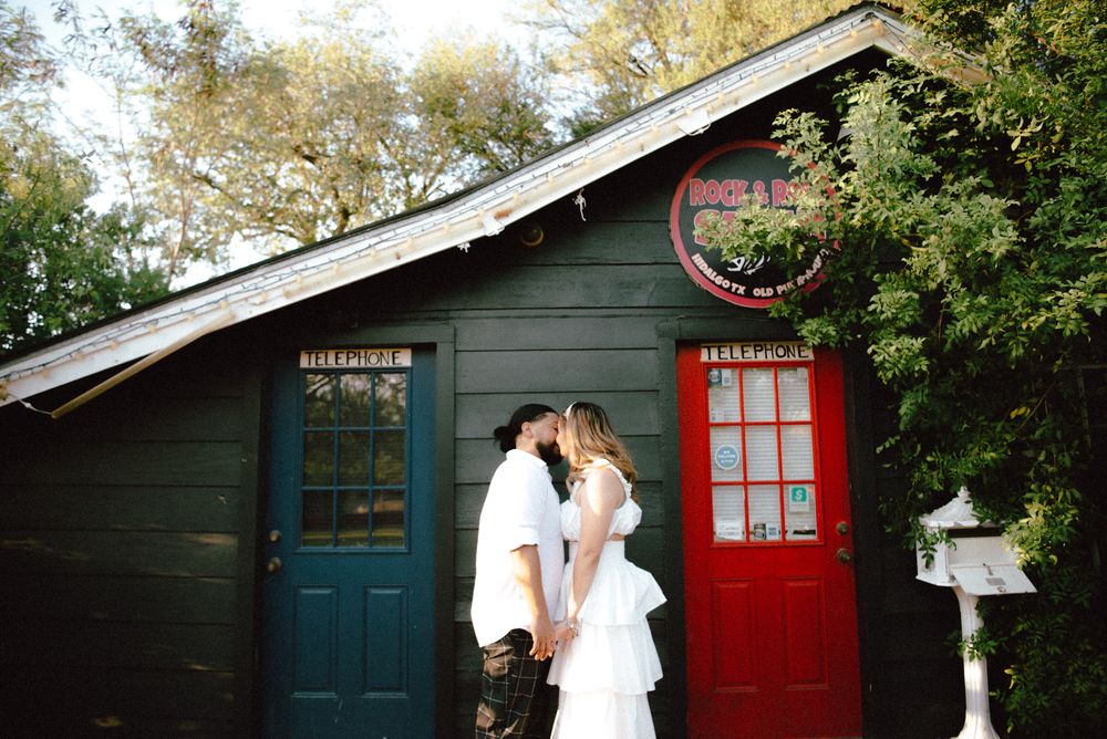 A couple embraces in front of a charming garden shed with contrasting teal and red doors.