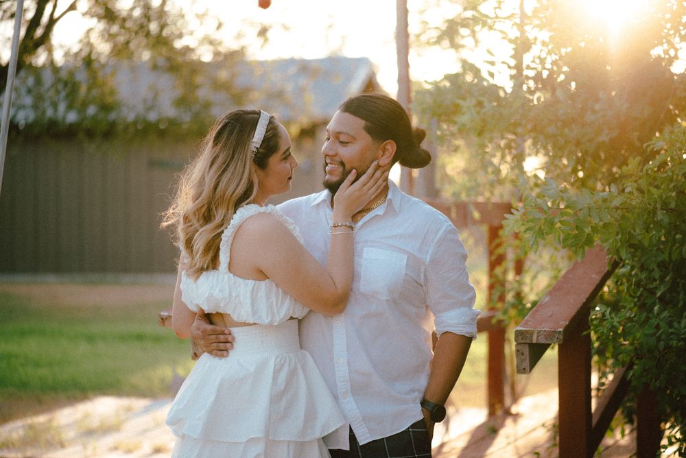 A romantic couple embraces in golden sunlight during sunset in a garden setting.