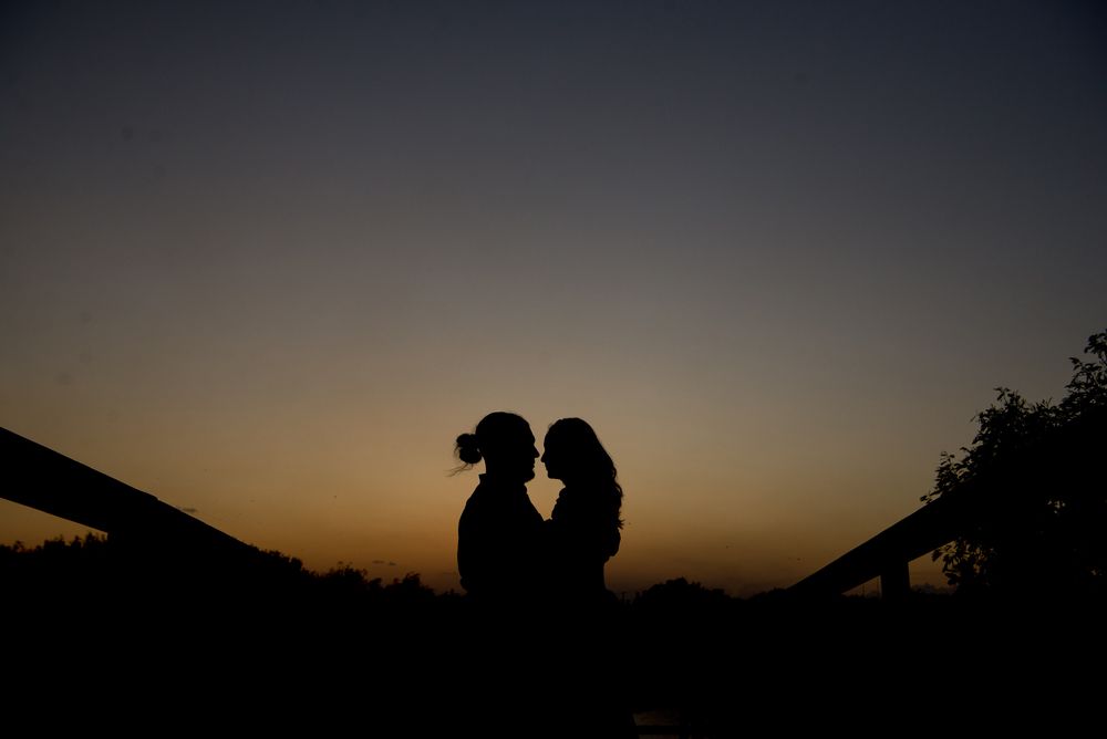 Romantic silhouette of two people embracing at sunset against a dusky orange sky.