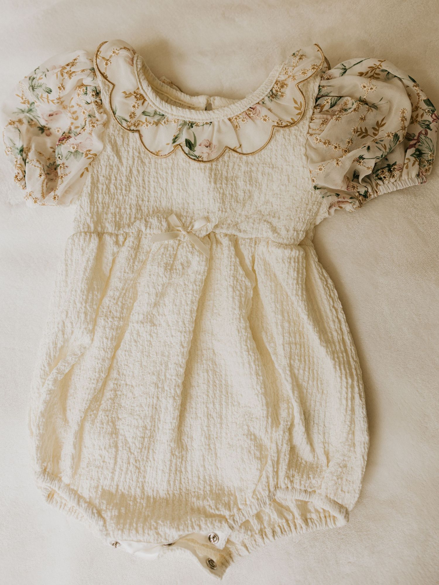 Stylish kids outfit featuring gray button-down shirt with floral bow tie, navy suspenders and khaki shorts.