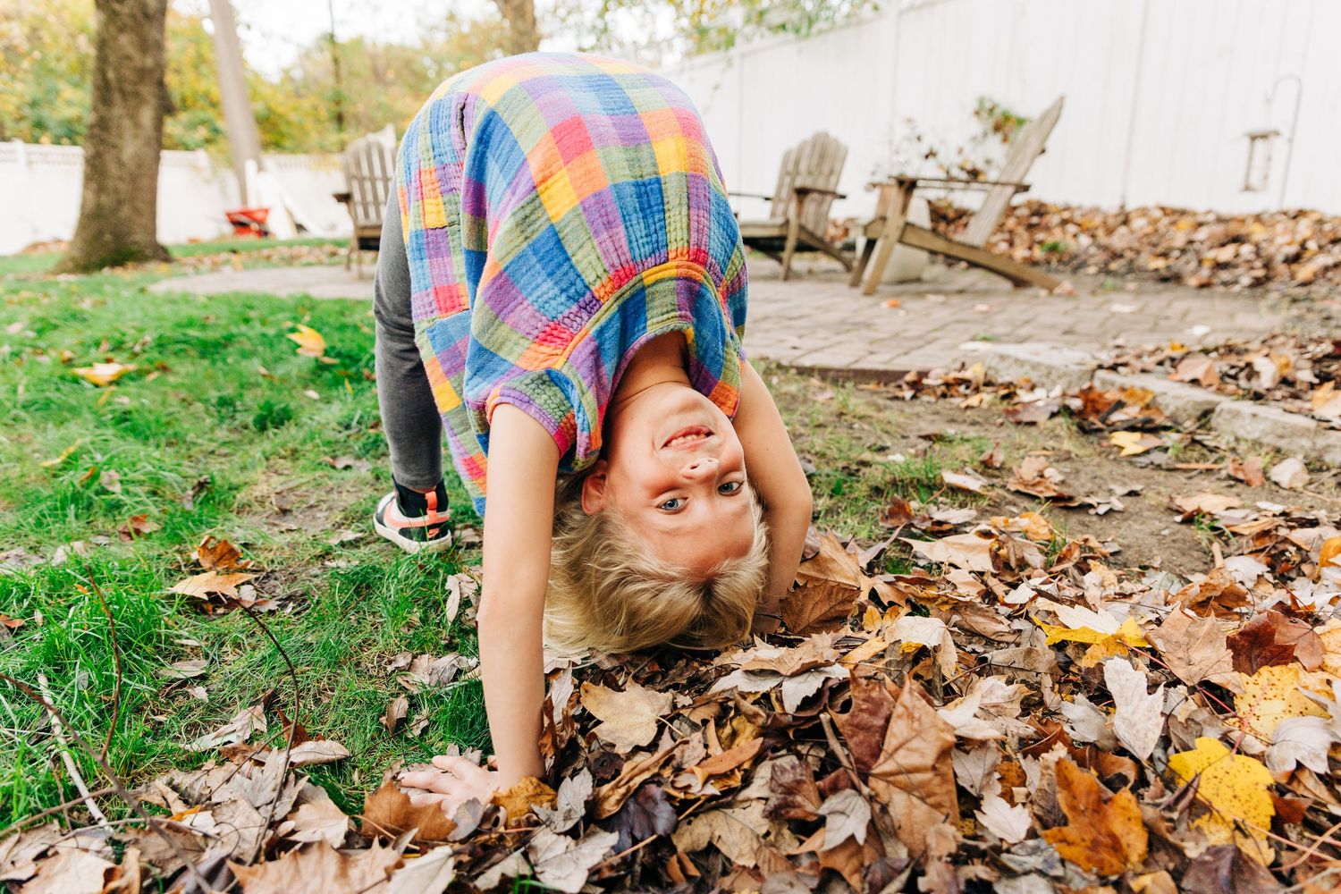 A young girl doing a back bend and smiling while playing in a pile of autumn leaves on a sunny day in Charlotte, NC.
